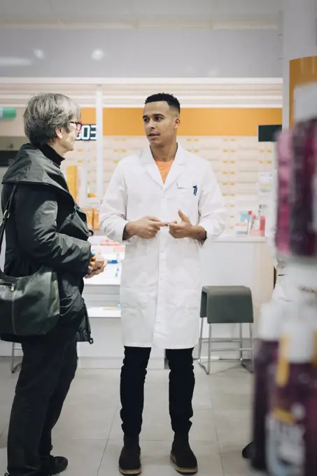 Full length of male pharmacist talking with senior female customer in medical store