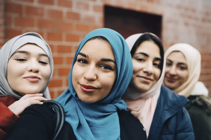 Portrait of smiling Muslim friends against building in city