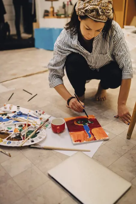 Female artist painting on paper while crouching at art studio