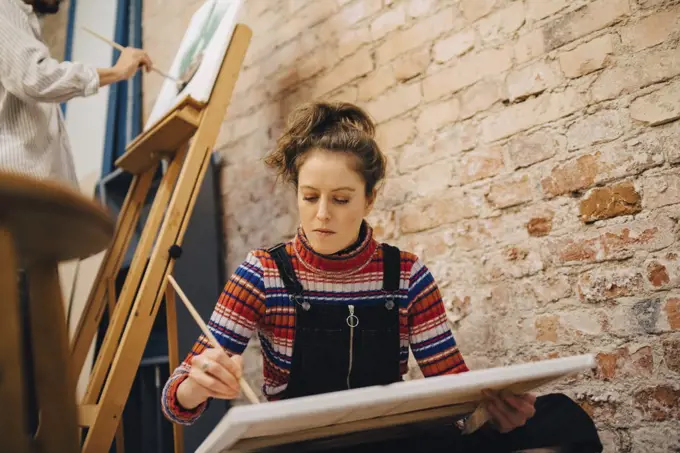 Low angle view of female and male artists painting on canvas at art studio