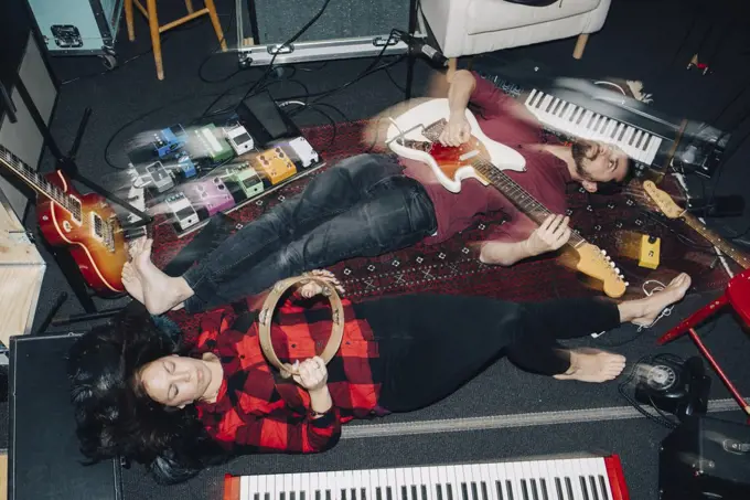 High angle view of male and female friends playing instruments while lying on floor at studio