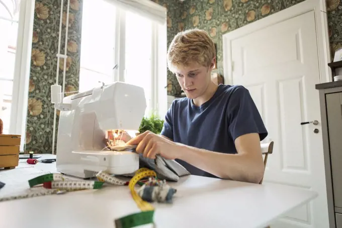 Young man sewing textile at home