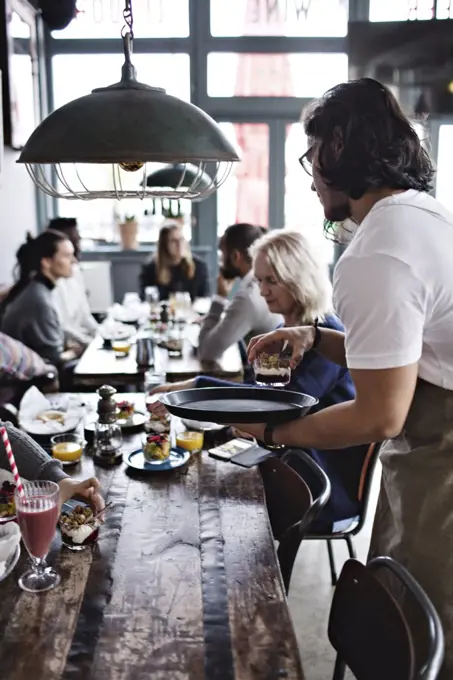 Waiter serving dessert to customers on dining table