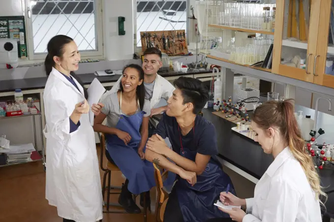 Happy mature teacher explaining to young multi-ethnic university students sitting in chemistry laboratory