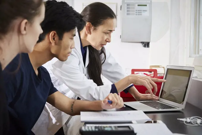 Teacher pointing at laptop screen to young engineering students in classroom