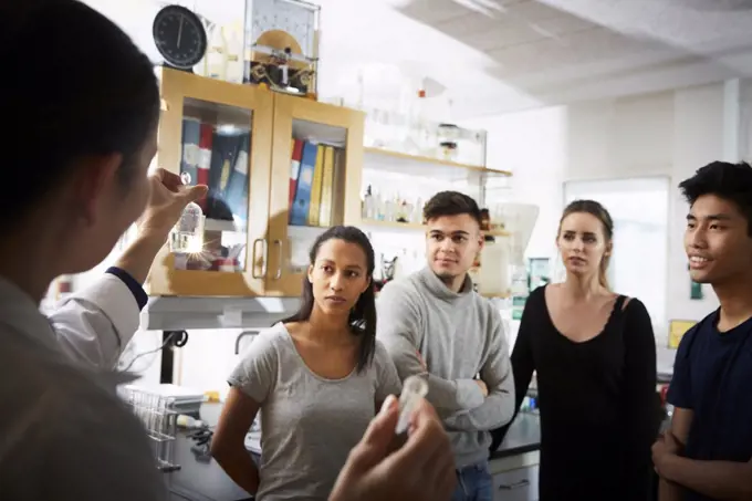 Rear view of mature female teacher showing solution while explaining to young multi-ethnic students in laboratory