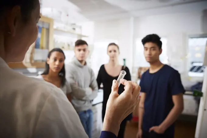 Rear view of mature female teacher holding test tube explaining to young multi-ethnic students in laboratory