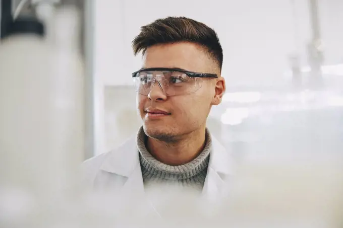 Confident young chemistry student wearing eyewear looking away in laboratory