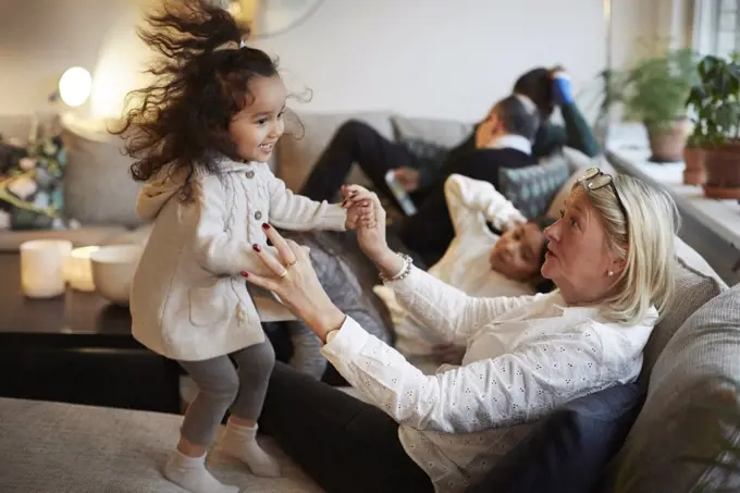 Girl playing with grandmother on sofa by family at home