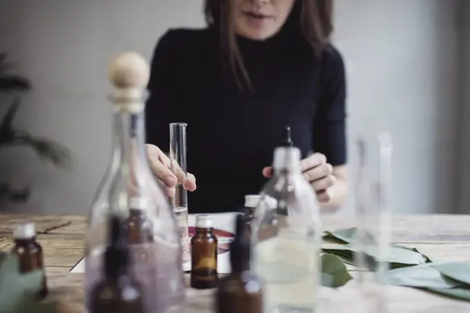 Midsection of female owner mixing liquid while sitting at table against wall in perfume workshop