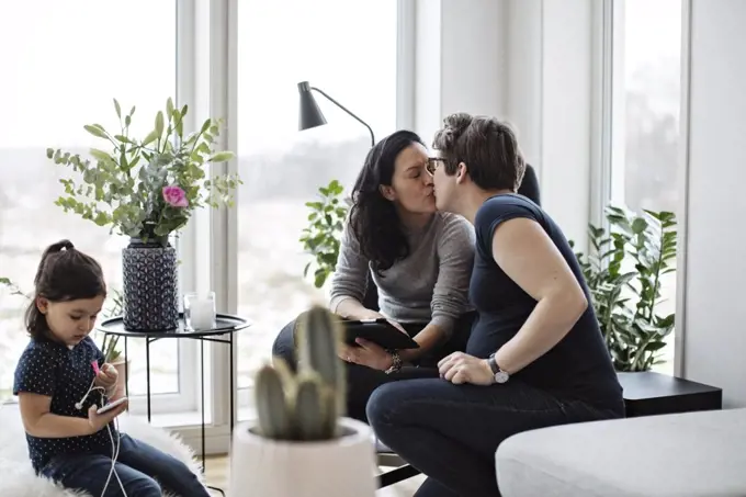 Lesbian couple kissing while girl using mobile phone in living room at home