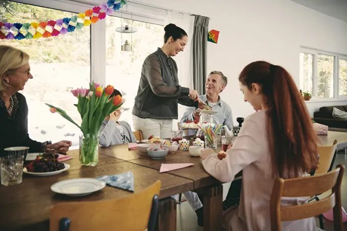 Smiling woman serving food to family during birthday party