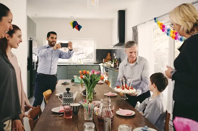 Man photographing boy with family during birthday party through smart phone