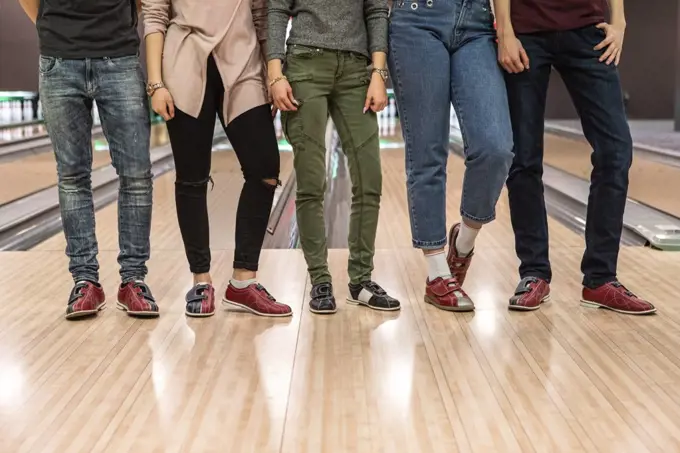 Low section of multi-ethnic friends standing on parquet floor at bowling alley