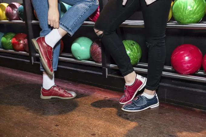 Low section of female friends wearing shoes standing by bowling rack