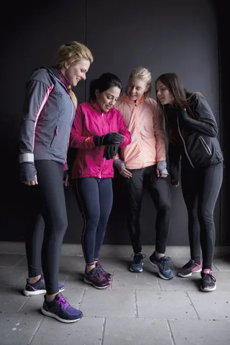 Full length of woman showing smart watch to friends while standing against wall in winter