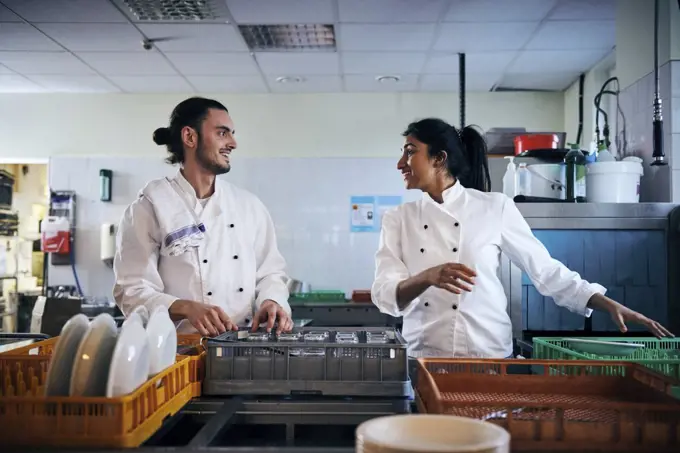 Male and female chefs communicating while arranging utensils in kitchen