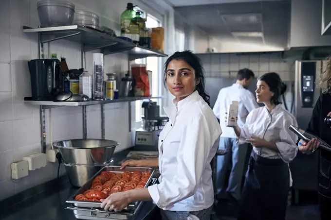 Portrait of chef with tomatoes in baking sheet at commercial kitchen