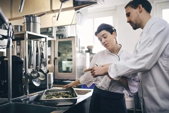 Male and female chefs reading order ticket while preparing food in commercial kitchen