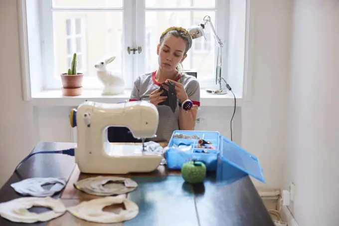 Tailor sewing scarf on machine while sitting against window at home