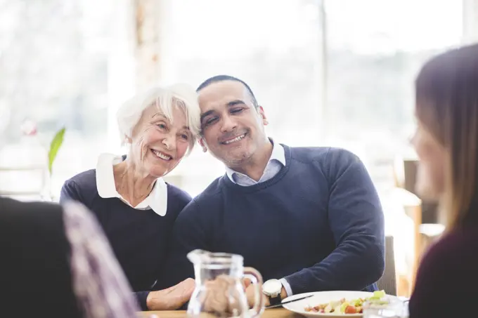 Smiling senior woman sitting with son while having lunch at table in nursing home