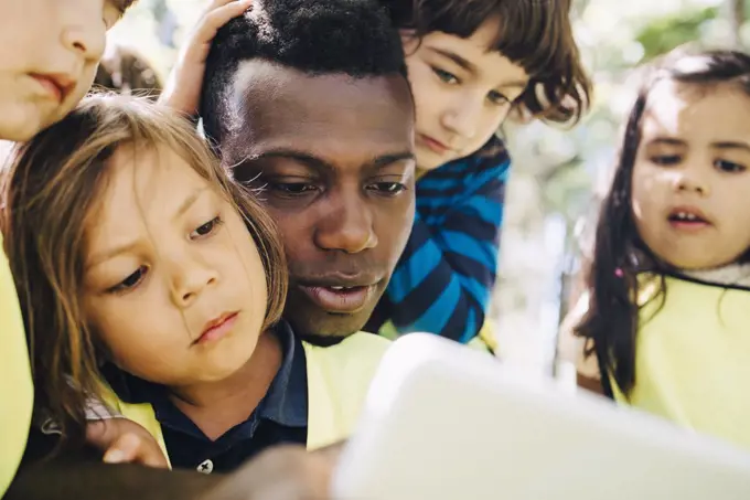 Male teacher sharing digital tablet with students in playground