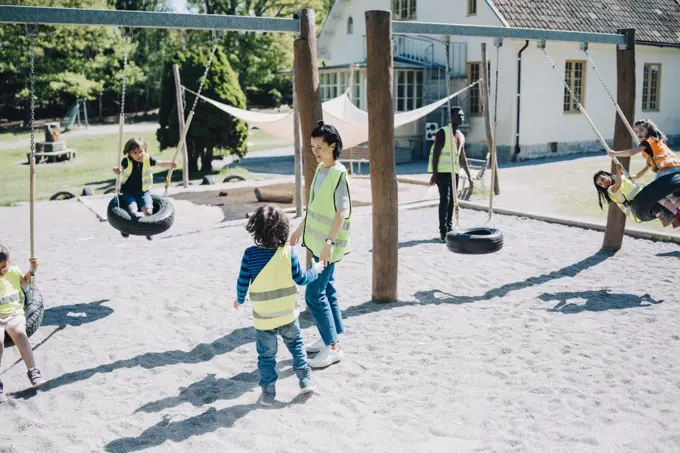 Teachers standing while students enjoying on swing in playground