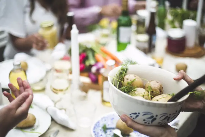 Cropped image of woman holding boiled potatoes bowl at dining table during dinner party