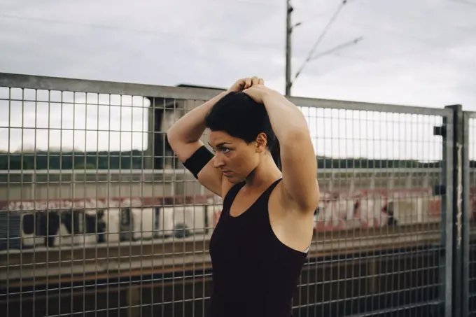 Determined female athlete tying hair while standing by fence on footbridge