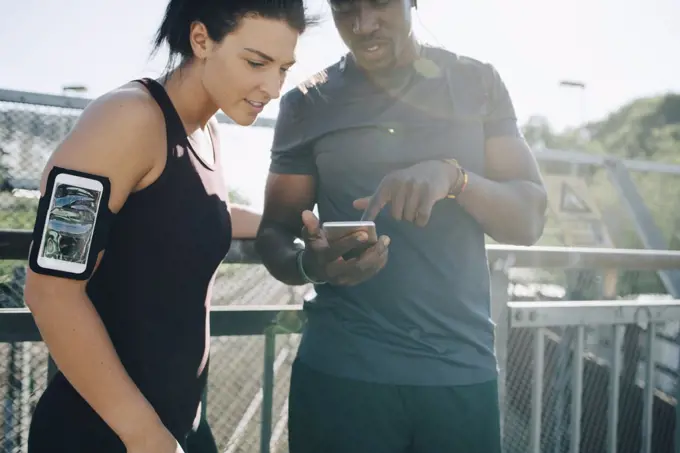 Sportsman showing mobile phone to female athlete while standing by railing on bridge