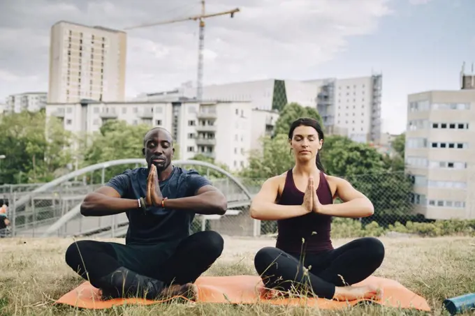 Multi-ethnic friends practicing yoga on field against buildings in city