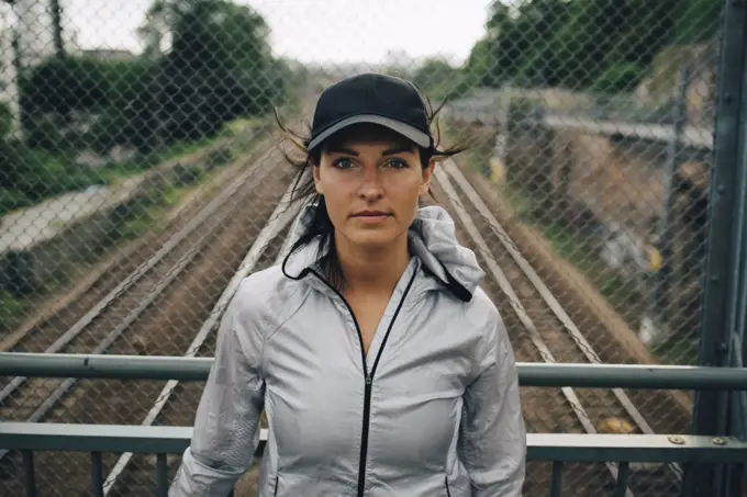 Portrait of confident female athlete standing against railing on bridge