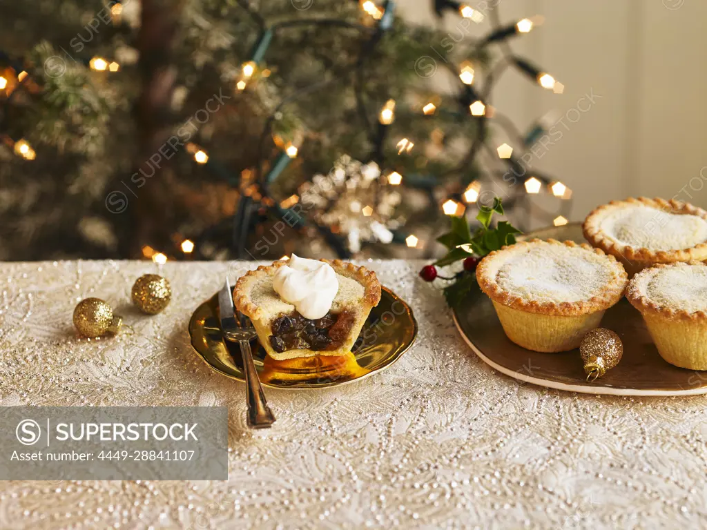 A plate of filled mince pies and one mince pie cut open with a dollop of cream