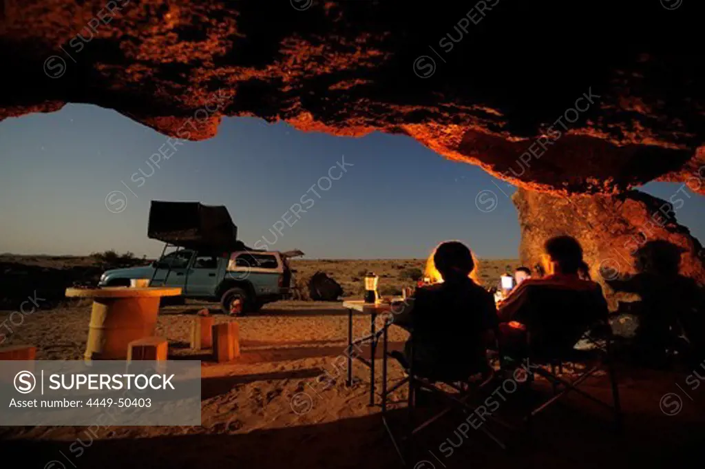 Group of people sitting under overhang, car with roof tent in background, stone desert, Namib Naukluft National Park, Namib desert, Namib, Namibia