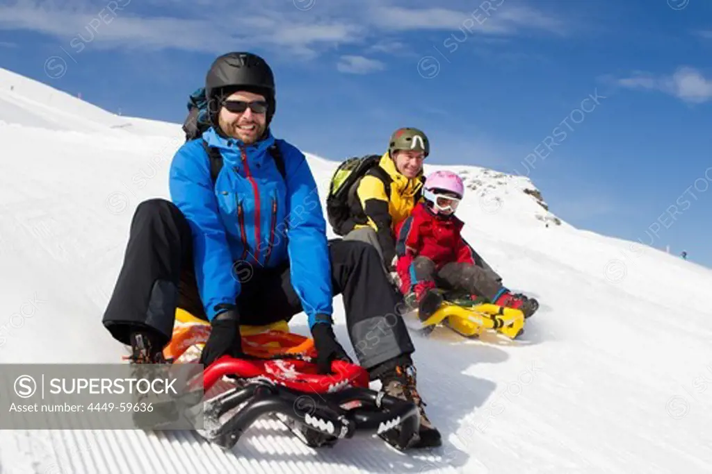 A girl and two men tobogganing on the toboggan run at ski resort Stoos, Kanton Schwyz, Switzerland