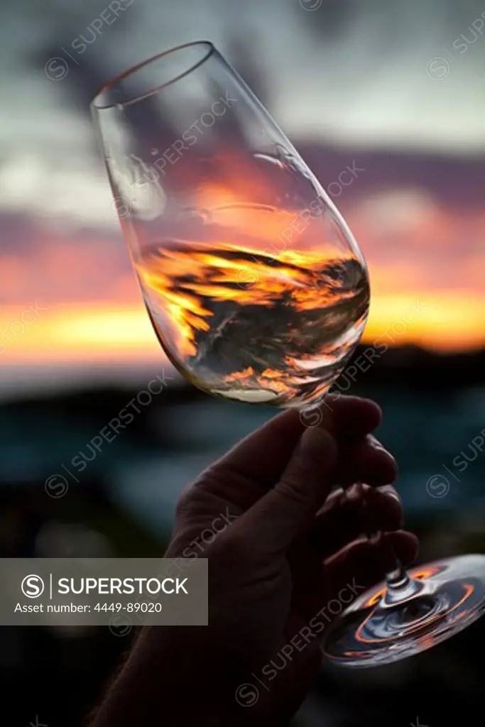 Hand holding and swirling glass of white wine against sunset, Stellenbosch, Western Cape, South Africa