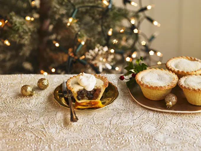 A plate of filled mince pies and one mince pie cut open with a dollop of cream