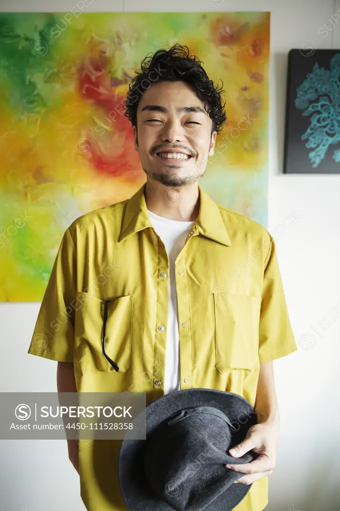 Japanese man standing in front of abstract painting in an art gallery, smiling at camera.