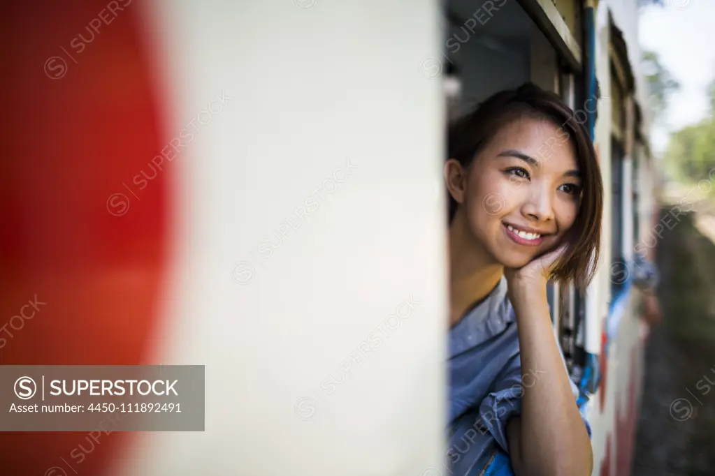 Smiling young woman riding on a train, looking out of window.