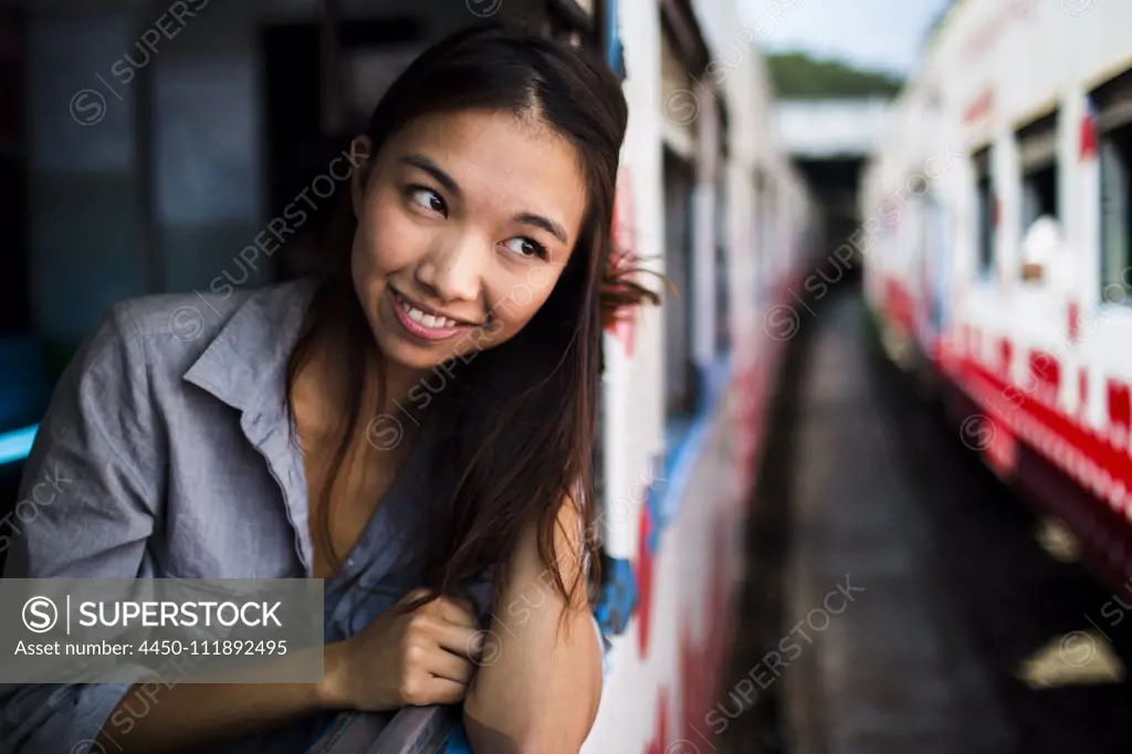 Smiling young woman riding on a train, looking out of window.