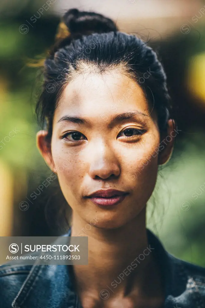 Portrait of a young woman with black hair tied in a top knot, looking at camera.