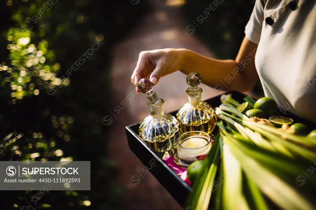 High angle close up of woman holding tray with glass bottles, candles and fruit.