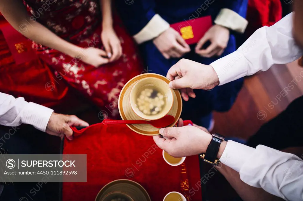 High angle close up of a ritual at a Chinese wedding ceremony, people passing a bowl of soup.