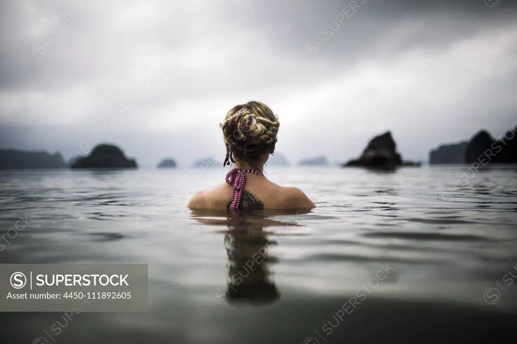 Rear view of woman with blond braided hair wading into the ocean.