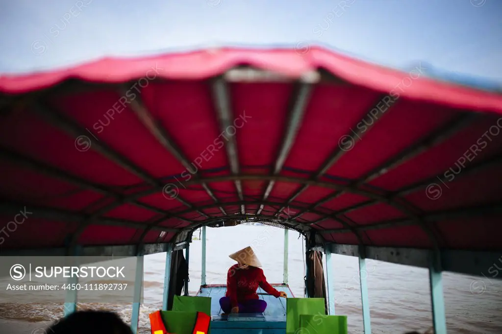 Woman piloting a boat with red canopy through a river.