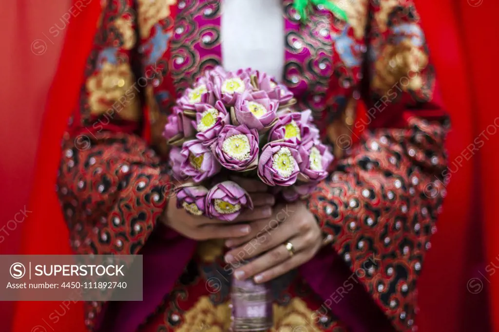 Close up of young Vietnamese bride wearing a colourful robe, holding a bouquet of lotus flowers.