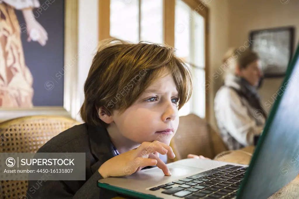 A six year old boy typing on a laptop at home, using the cursor touch pad. 