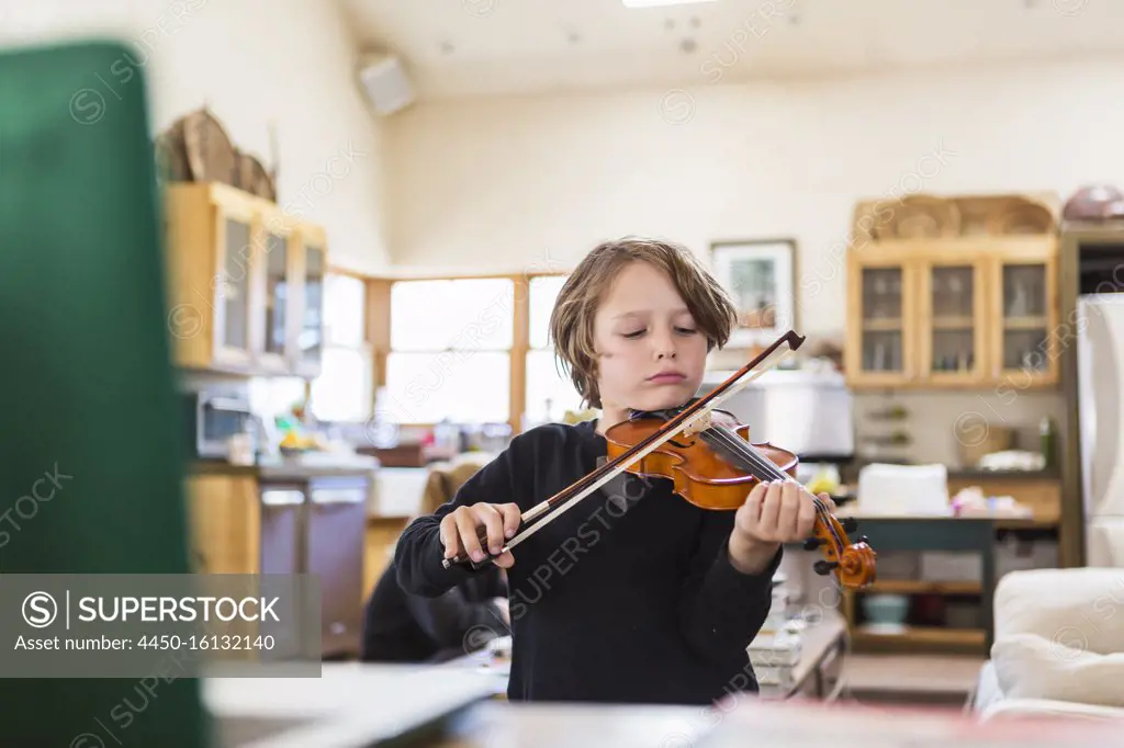 Six year old boy playing violin, having a remote video lesson in lockdown at home. 