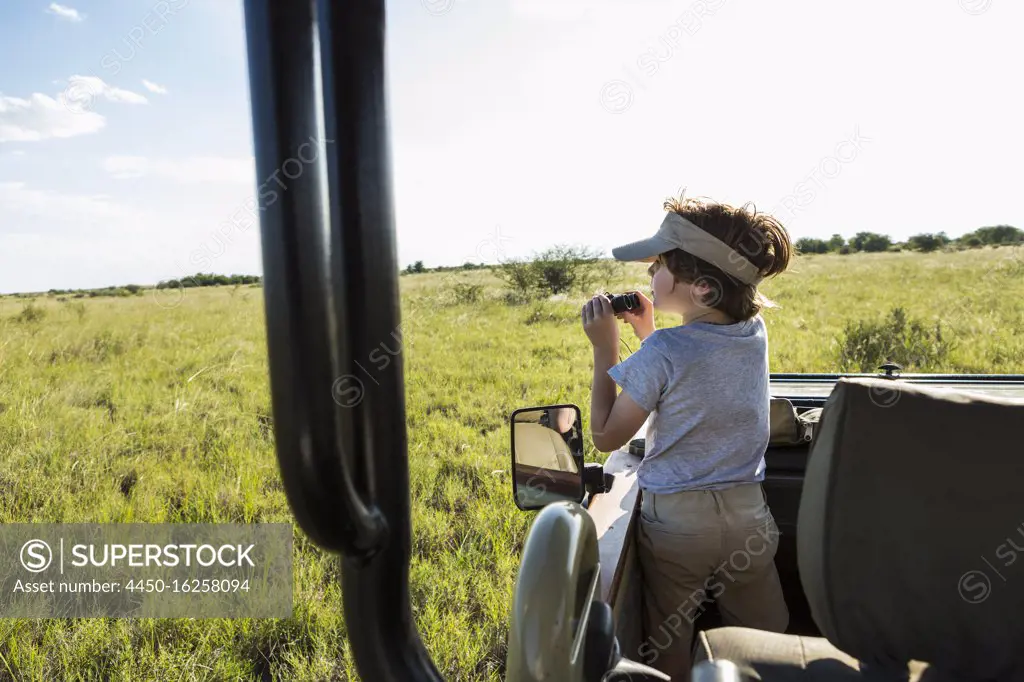 A six year old boy with binoculars in a safari vehicle