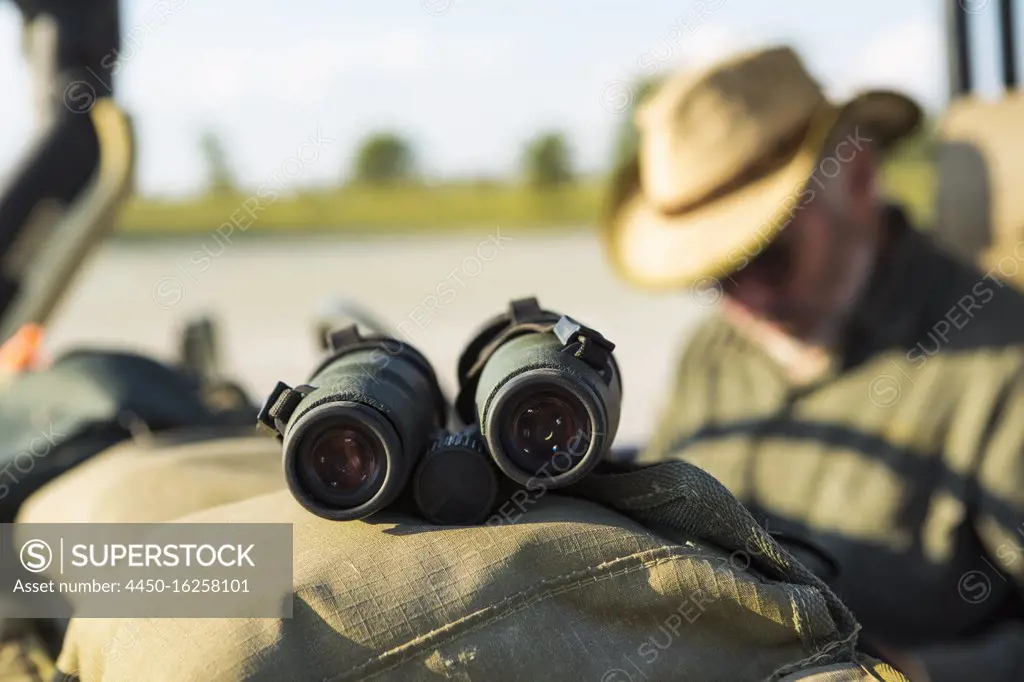 Binoculars on the dash of a safari jeep, a safari guide in the background. 